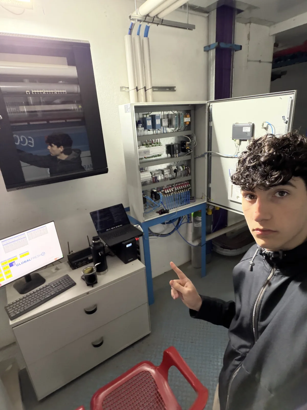Faustino junto a un tablero industrial abierto y las computadoras de trabajo.